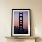 Framed artwork of the Golden Gate Bridge silhouette against a purple sky on a white wall.