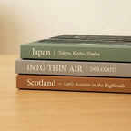 Three books titled 'Japan', 'Into Thin Air', and 'Scotland' on a wooden surface.