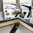 Close-up of a metal and wood trim molding machine with vertical metal arms pressing down on a V-shaped piece of wood trim to shape it.